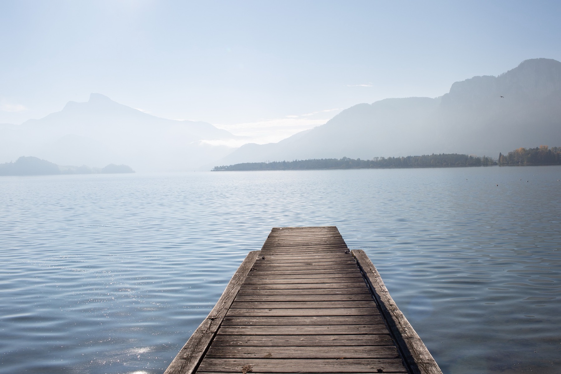 Embarcadero de madera sobre un lago en calma, con montañas al fondo